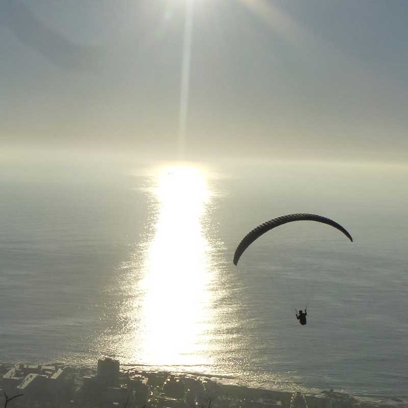 Paraglider gleitet vor einer Küste dem Sonnenuntergang entgegen